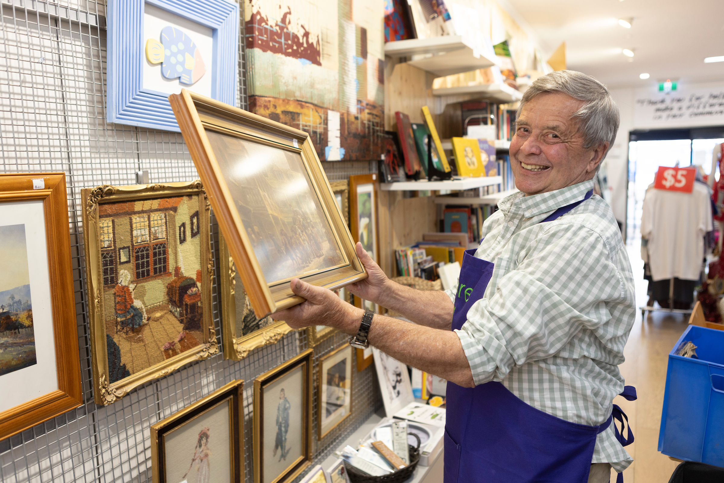 A older man in the Norwood Elcies is hanging up painting in the op shop
