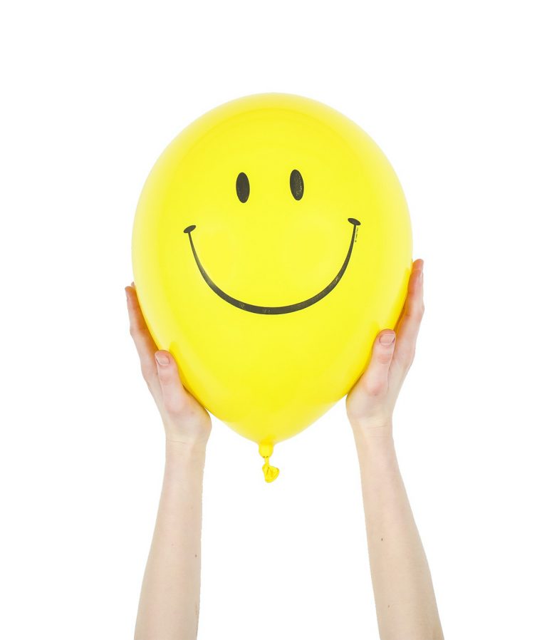 Image of two hands holding up a yellow balloon with a smiling face on it