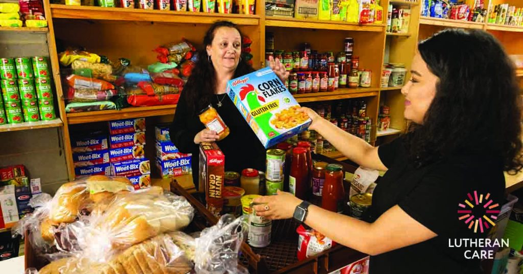Two women are organising donated food items in the Lutheran Care Emergency Relief pantry. The Lutheran Care logo appears in the bottom right hand corner.