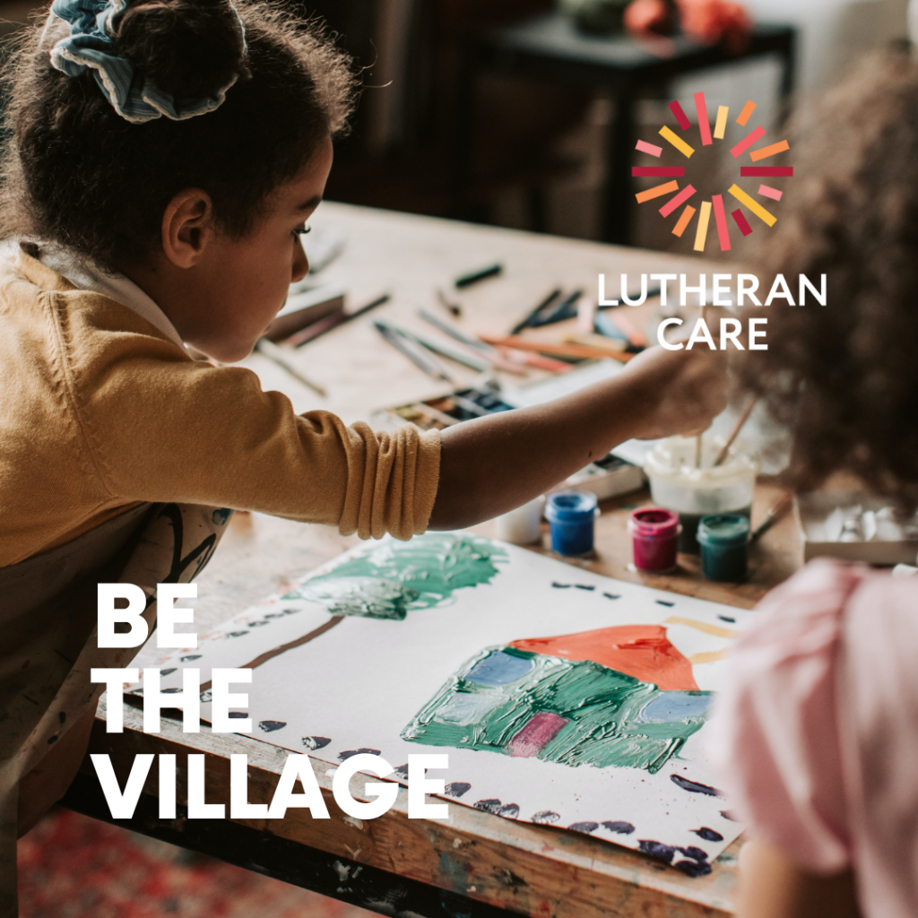 Two children are painting a picture of a house. The text logo at the bottom of the image reads Be the Village and appears with the Lutheran Care logo