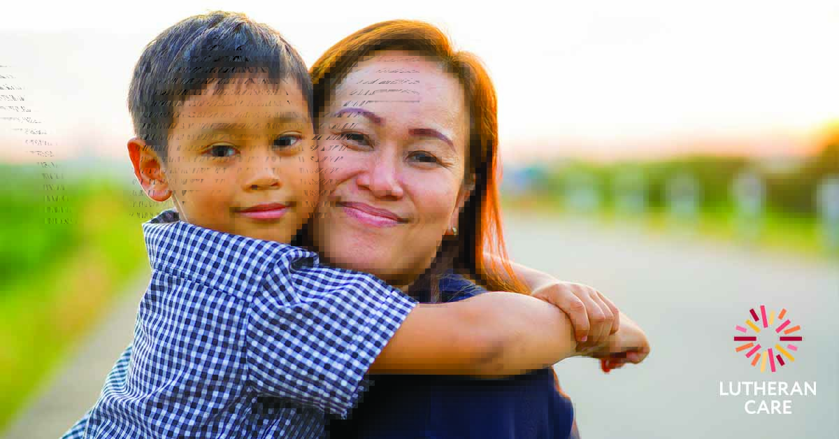 A young boy is hugging his mother as she holds him in her arms both smiling at the camera. The Lutheran Care Logo appears in the bottom right hand corner