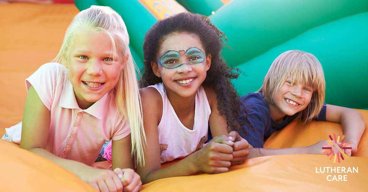 Image of three children on a bouncy castle smiling at camera. The Lutheran Care logo appears in the bottom right hand corner.