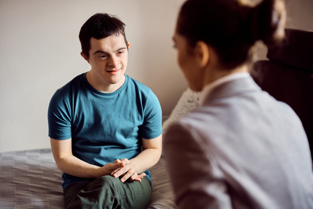 Young man with down syndrome chats with his therapist talking during home visit.
