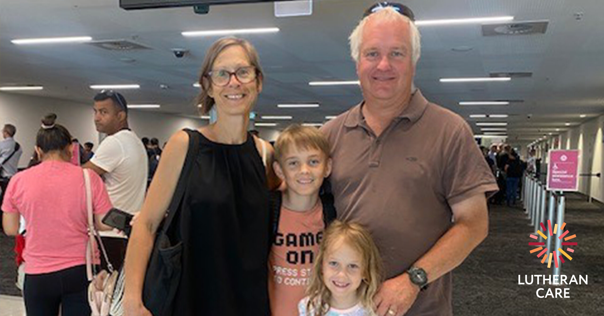 Susie and Graeme with their children at the airport. The Lutheran Care logo appears in the bottom right hand corner.