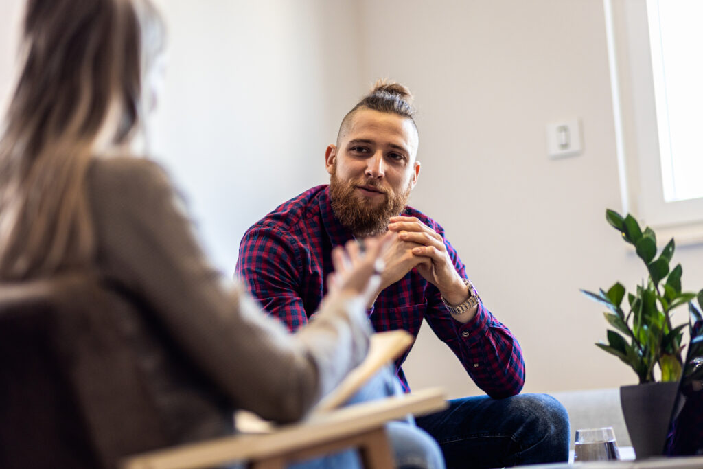 A man is speaking with a female psychologist in a therapy session.