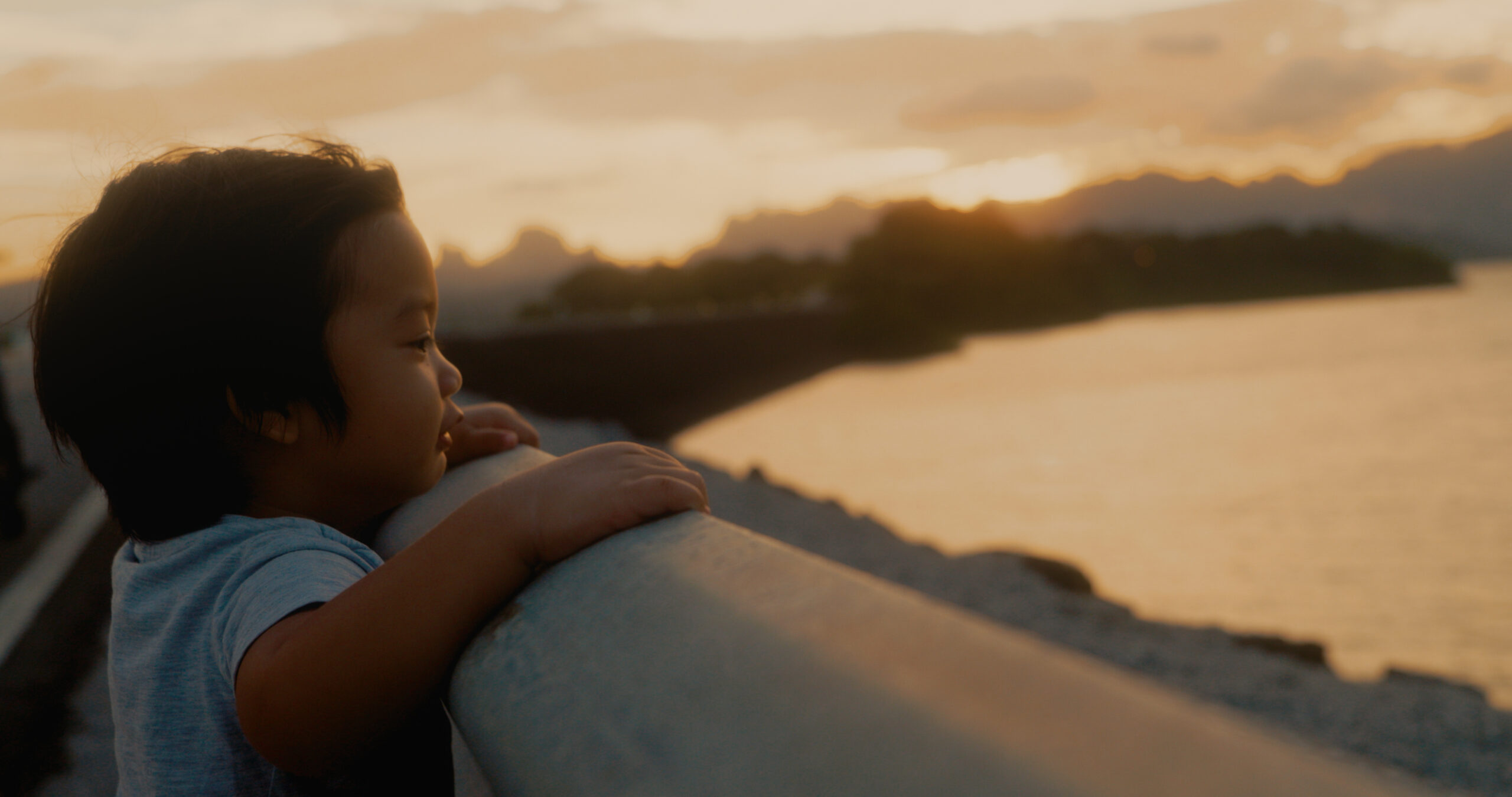Young boy watches the sunrise on a bridge.