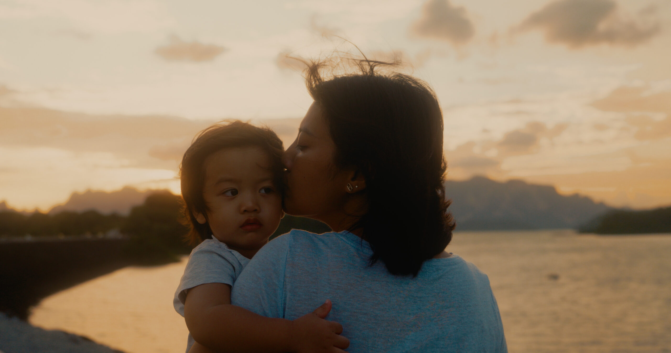 A mother holds son up to watch the sunset at the dam.