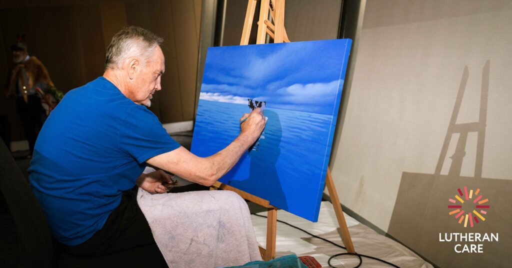 Image of Andrew Baines painting at the 2023 Lutheran Care Gala Dinner. The Lutheran Care logo appears in the bottom right hand corner.