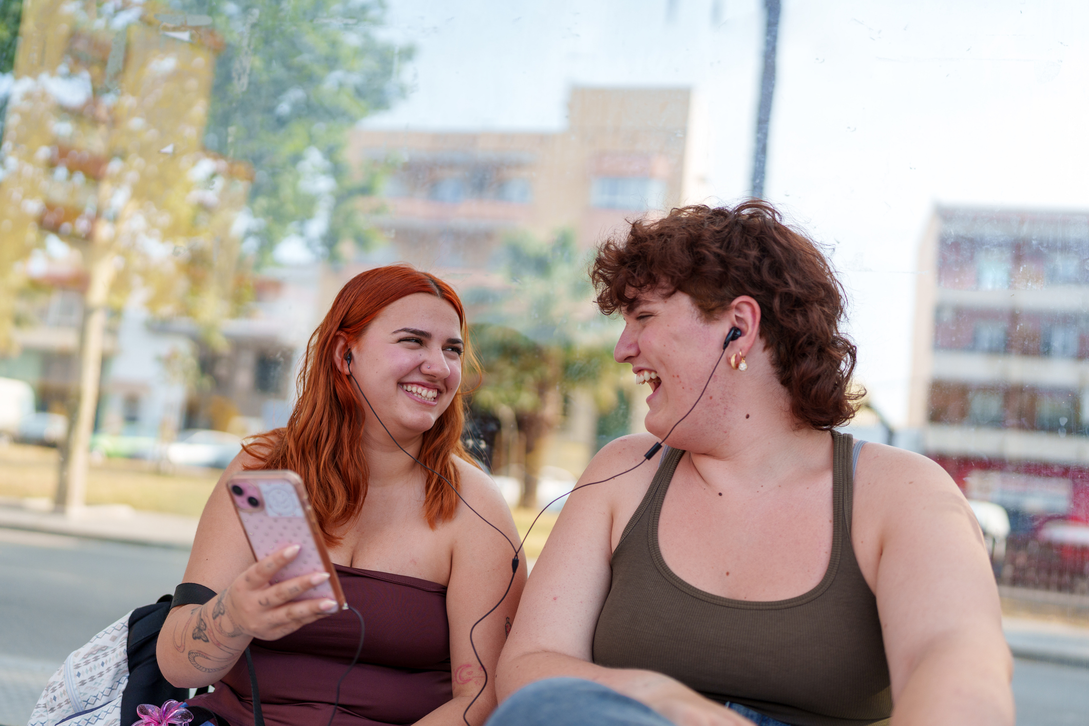 Two young people laugh together outside at something on a mobile phone.