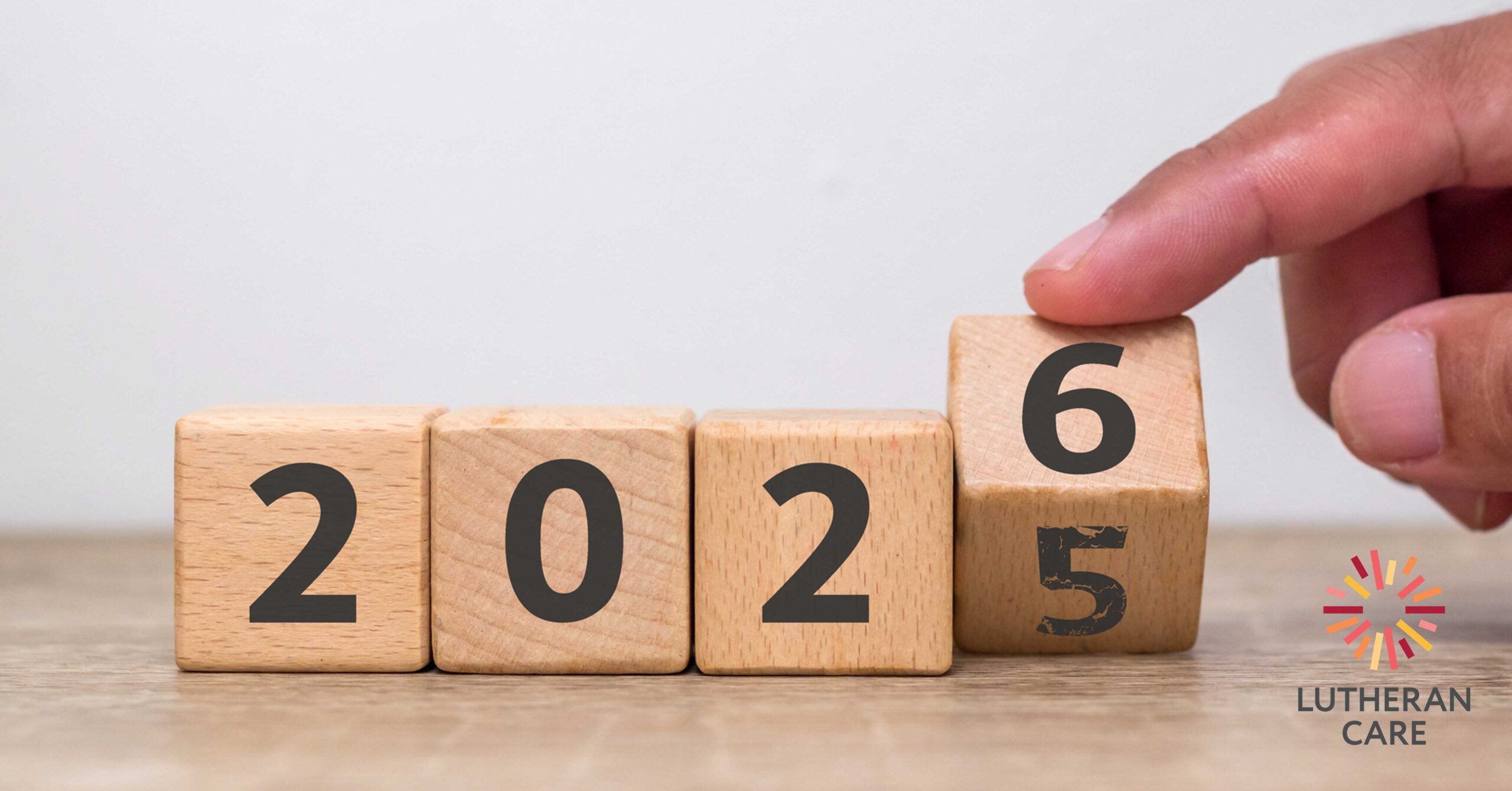 Image of wooden blocks with 2025 on them someone is moving the 5 to 6 to reflect going into the year 2026. The Lutheran Care logo appears in the bottom right hand corner.