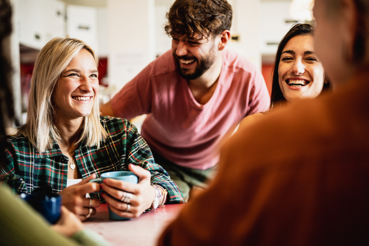 A group of people laughing together whilst drinking coffee at a table.