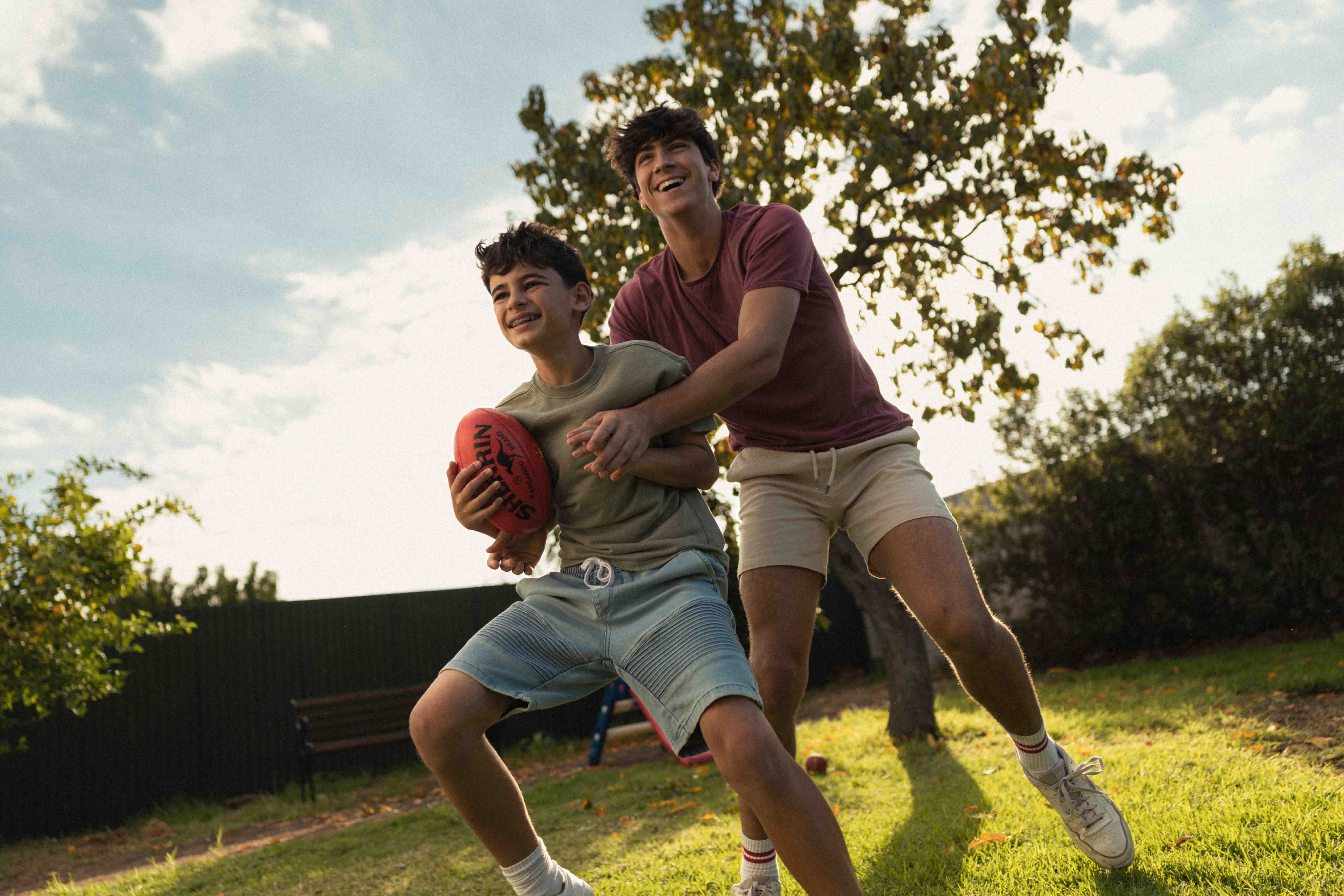 Two teenage boys laughing and playing football in the back garden.