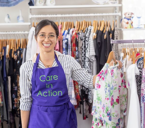 An Op Shop volunteer wearing a purple apron with 'Care in Action' embroidered on it with some of the ladies' clothes at our Blair Athol Op Shop.