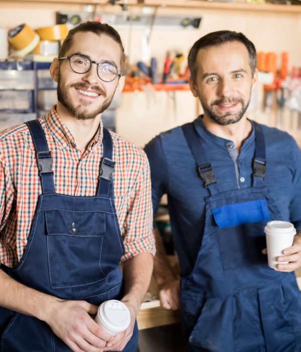 Waist up portrait of two smiling men in a workshop looking at camera while taking break.