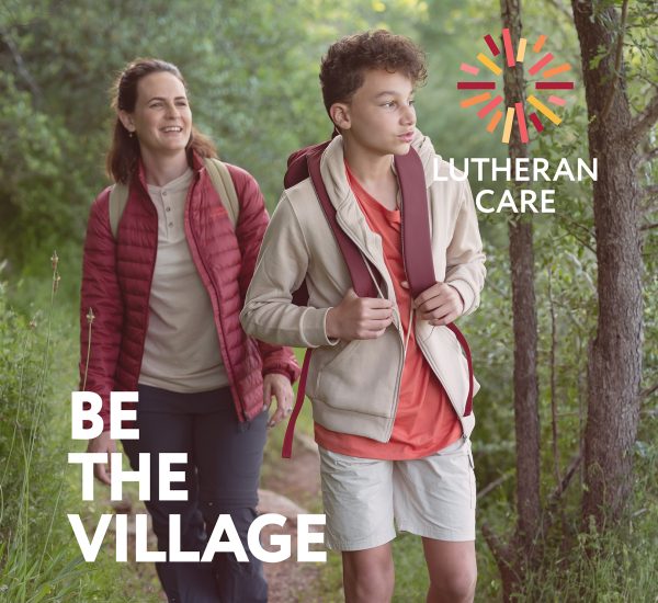 Woman and a teenage boy walk on a hike outside. Text says Be The Village and the Lutheran Care logo appears in the top right hand corner.