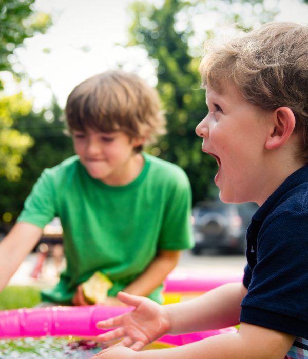 Image of two boys playing together outside. The boy closest to the front is laughing at something outside of the image.