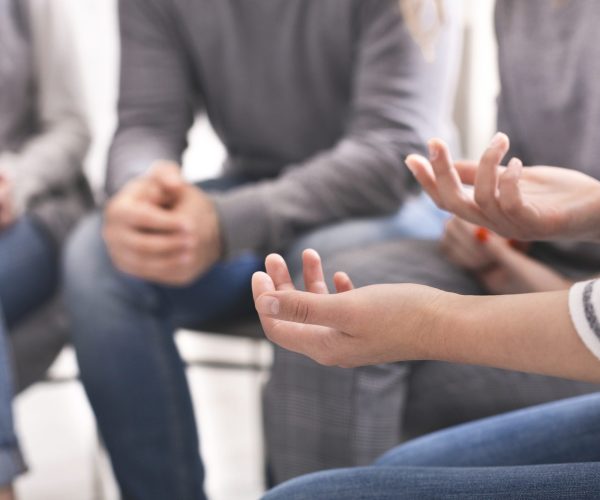 A group of people sit together in a counselling session as a woman is gesturing with her hands as she speaks.