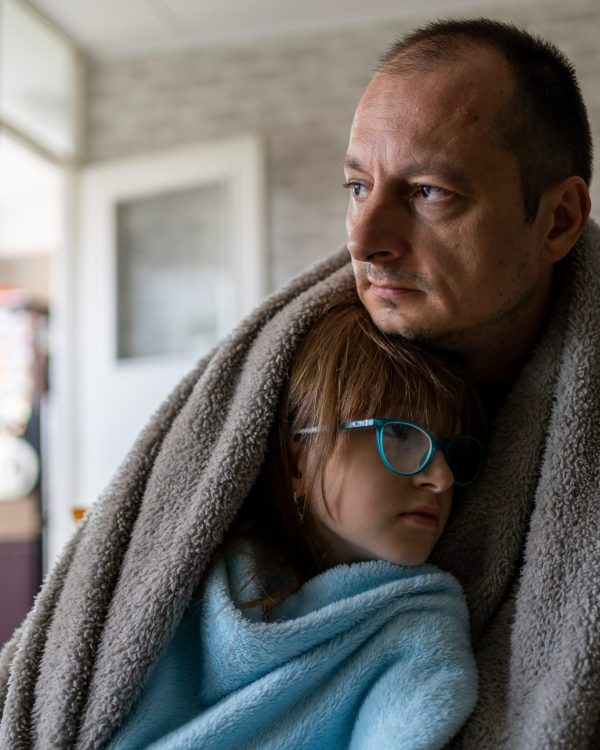 Father and his daughter hug with a blanket around them to stay warm.