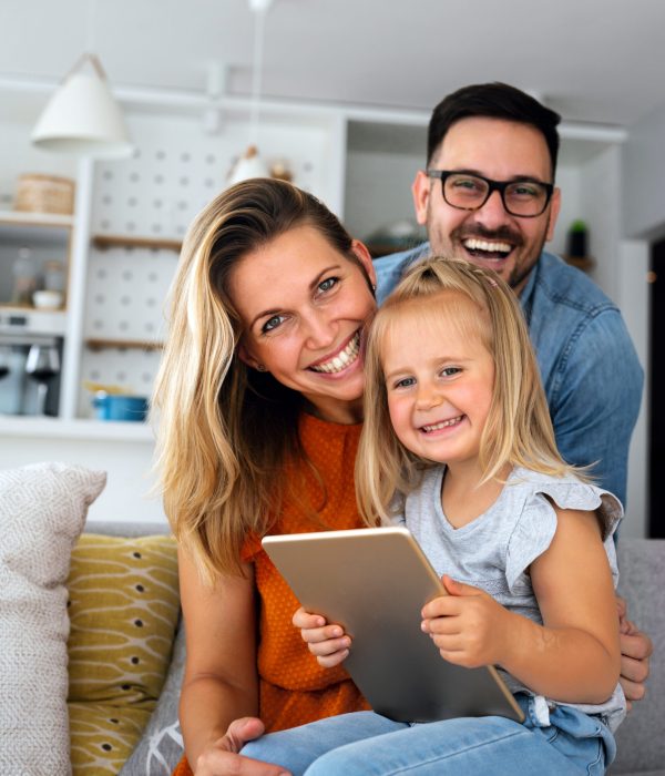 Parents and their young daughter smile for photo in their home, the young girl is holding a digital tablet