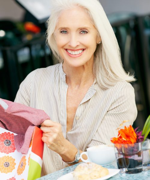 Senior Woman Enjoying Snack At Outdoor Café After Shopping